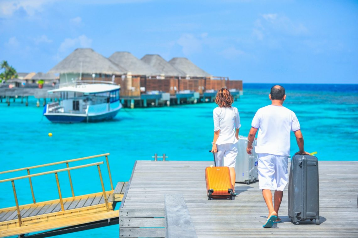 a man and a woman walking to the blue sea beach with luggage